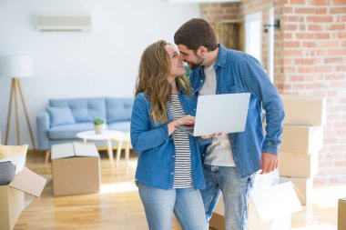 Yeni bir daireye taşımak için mutlu karton kutular etrafında bir odada bilgisayar laptop ayakta kullanarak genç çift