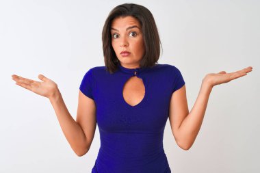 Genç güzel kadın mavi zarif t-shirt izole beyaz arka plan üzerinde duran giyen habersiz ve kolları ve elleri ile karışık ifade kaldırdı. Şüphe kavramı.