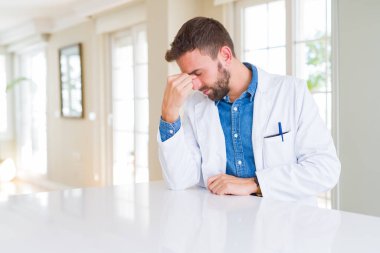 Klinikte tıbbi palto giyen yakışıklı doktor, burun ve gözleri sürtünme yorgun yorgunluk ve baş ağrısı hissi. Stres ve hayal kırıklığı kavramı.
