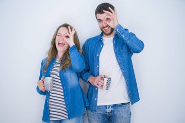 Genç güzel çift mutlu yüz parmakları ile bakarak göz el ile ok işareti yapıyor gülümseyerek beyaz izole arka plan üzerinde bir fincan kahve içme