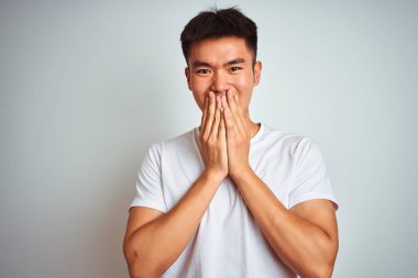 Genç asyalı Çinli adam izole beyaz arka plan üzerinde duran t-shirt giyen gülme ve elleri, dedikodu ve skandal kavramı ile ağız kapsayan kıkırdama utandım