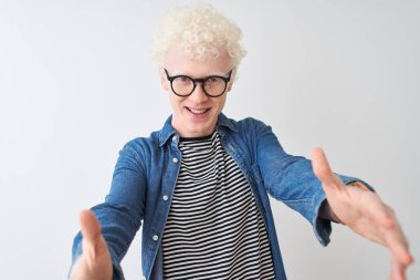 Genç albino sarışın adam denim gömlek ve gözlük giyen izole beyaz arka plan üzerinde sarılmak için açık kollarla gülümseyen kameraya bakarak. Mutluluğu kucaklayan neşeli ifade.