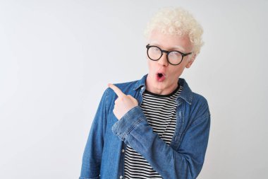 Genç albino sarışın adam denim gömlek ve gözlük giyen izole beyaz arka plan üzerinde yan parmak ile işaret şaşırttı, açık ağız hayrete ifade.