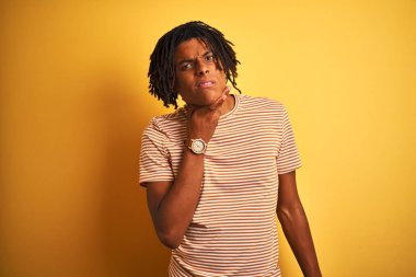 İzole sarı arka plan üzerinde duran çizgili t-shirt giyen dreadlocks ile Afro adam ağrılı boyun dokunmadan, grip, clod ve enfeksiyon için boğaz ağrısı