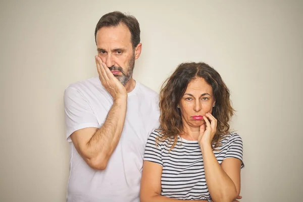 Beautiful middle age couple together standing over isolated white background thinking looking tired and bored with depression problems with crossed arms.