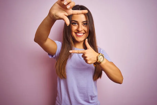 年轻美丽的女人穿着休闲的T恤 站在孤立的粉色背景上 微笑着 用双手和手指做着幸福的框架 创意和摄影概念 — 图库照片