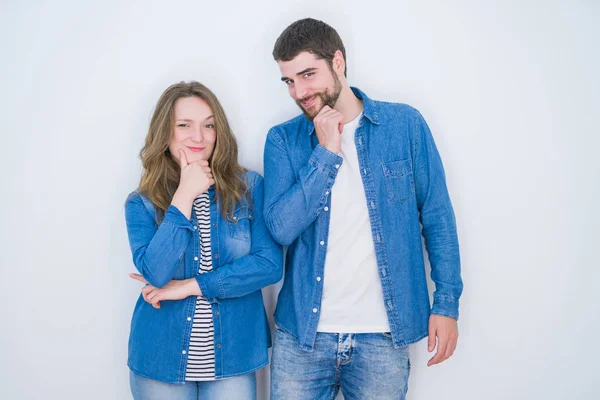 Young beautiful couple standing together over white isolated background looking confident at the camera with smile with crossed arms and hand raised on chin. Thinking positive.