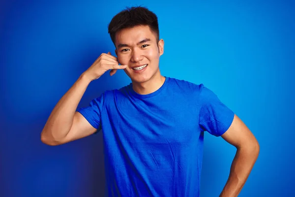 孤立した青い背景の上に立つTシャツを着たアジアの若い中国人男性は 電話で話すような手と指で電話ジェスチャーをして微笑んでいます 概念の伝達 — ストック写真