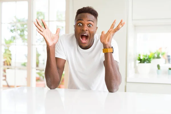 自宅の白いテーブルの上のハンサムなアフリカ系アメリカ人の男性は 腕を上げ 目を開けて興奮して成功を祝いました 勝者のコンセプト — ストック写真