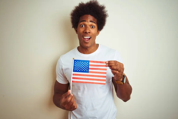 Afro man holding United Estates of America USA flag standing over isolated white background scared in shock with a surprise face, afraid and excited with fear expression