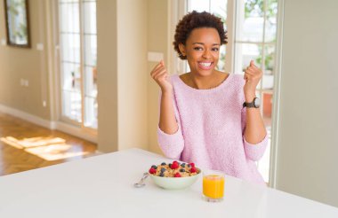 Sabah ları evde sağlıklı kahvaltı yapan afro-amerikalı genç kadın, kollarını kaldırıp gözleri açık bir şekilde başarıya uğrup büyülemesine neden oldu. Kazanan kavramı.