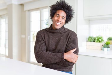 Kış lık kazak giyen Afro-Amerikan adam mutlu bir yüz le gülümseyerek kameraya bakıyor çapraz kollarıyla. Pozitif kişi.