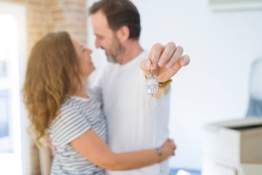 Orta yaş Senior romantik çift tutan ve ev anahtarlarını gösteren, sarılmak ve yeni bir eve taşımak için mutlu gülümseyen
