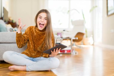 Güzel genç kız çocuk çok mutlu ve heyecanlı katta oturan dijital touchpad tablet kullanarak, büyük bir gülümseme ile çığlık zafer kutlayan kazanan ifade ve ellerini kaldırdı