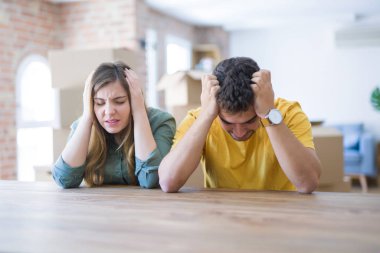 Masada oturan genç çift, arkalarında karton kutularla yeni eve dönerken baş ağrısı ndan muzdarip ve stresli çünkü ağrı ve migren. Eller baş üstünde.