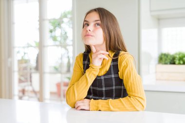 Genç güzel sarışın çocuk kız evde rahat sarı kazak giyen düşünme çene parmak ile şüphe hakkında konsantre ve merak yukarı bakıyor