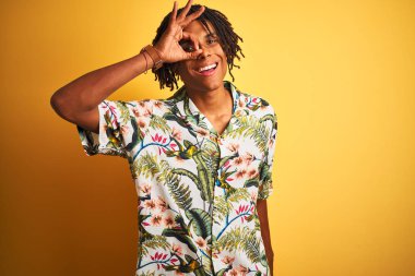 Tatilde dreadlocks ile Afro adam izole sarı arka plan üzerinde yaz gömlek giyen el gülümseyerek ok jest yapıyor, mutlu yüz ile parmakları ile bakan göz.