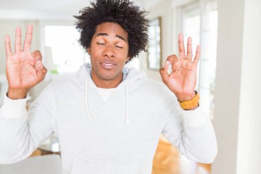 Afro-Amerikan adam sweatshirt giyen rahatlayın ve gözleri parmakları ile meditasyon jest yapıyor kapalı gülümseyerek. Yoga konsepti.