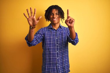 Kendinden emin ve mutlu gülümserken izole sarı arka plan üzerinde duran ve parmakları ile işaret eden rahat gömlek giyen dreadlocks ile Afro adam.