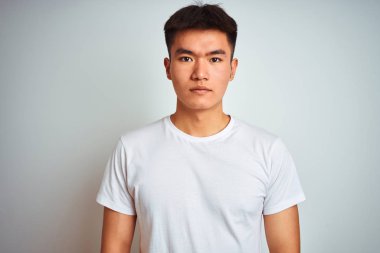 İzole beyaz arka plan üzerinde duran t-shirt giyen genç Asyalı Çinli adam yüzünde ciddi ifade ile rahat. Kameraya basit ve doğal bir bakış.