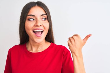 Genç, güzel bir kadın, kırmızı günlük tişört giyiyor, izole edilmiş beyaz arka plan üzerinde duruyor ve baş parmağıyla gülümsüyor.