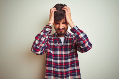 Genç adam rahat gömlek giyen izole beyaz arka plan üzerinde baş ağrısı umutsuz acı ve stresli çünkü ağrı ve migren üzerinde duran. Eller baş üstünde.