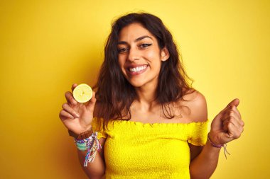 Genç güzel kadın izole sarı arka plan üzerinde duran orta limon tutan gurur çığlık ve zafer ve başarı çok heyecanlı kutluyor, duygu tezahürat
