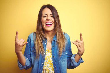 Genç güzel kadın elleri yukarı kaya sembolü yapıyor deli ifade ile bağırarak sarı izole arka plan üzerinde duran. Müzik yıldızı. Ağır müzik konsepti.