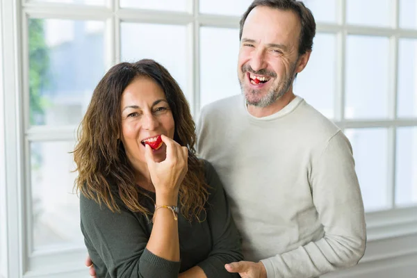 Middle age senior couple eating a fresh strawberry at home