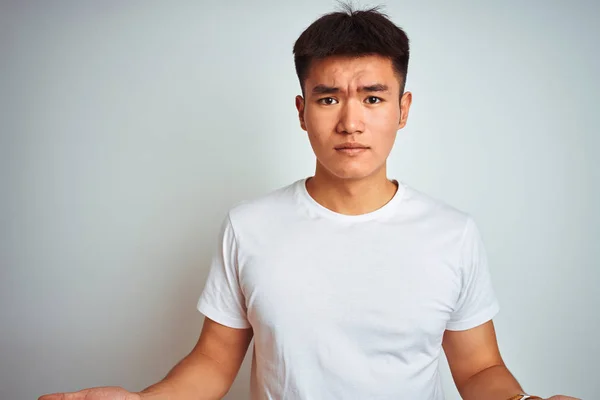 孤立した白い背景の上に立つTシャツを着た若いアジアの中国人男性は 開いた腕と混同し アイデアの概念を持っていません — ストック写真