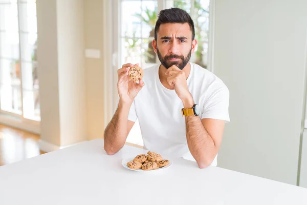 Stilig Spansktalande Man Äta Choklad Chips Cookies Allvarliga Ansikte Tänkande — Stockfoto