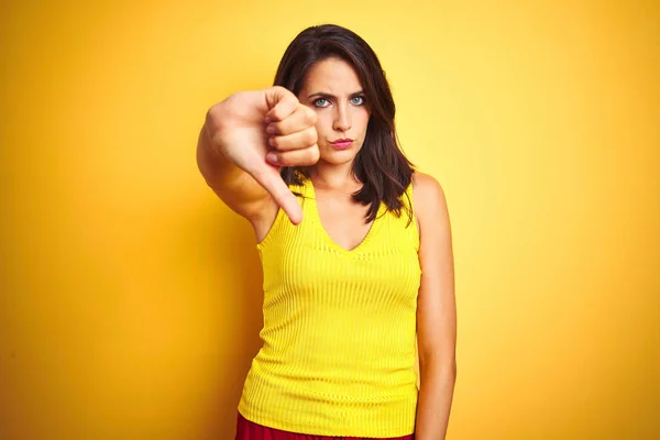 年轻的漂亮女人穿着T恤站在黄色孤立的背景看起来不高兴和愤怒显示拒绝和消极的拇指向下手势 表达错误 — 图库照片