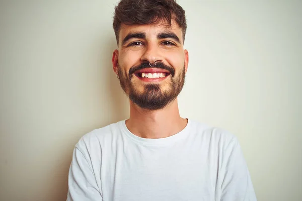 Young man with tattoo wearing t-shirt standing over isolated white background happy face smiling with crossed arms looking at the camera. Positive person.