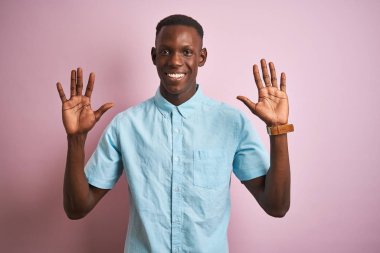 Izole pembe arka plan üzerinde duran mavi rahat gömlek giyen Afrikalı Amerikalı adam gösteren ve emin ve mutlu gülümserken parmakları on numara ile işaret.