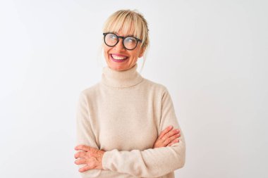 Orta yaş kadın boğazlı kazak giyen ve izole beyaz arka plan üzerinde gözlük yan bakarak gülümseyerek ve düşünme uzak bakıyor.