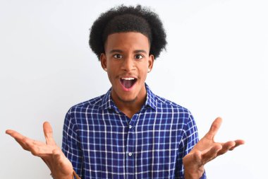 Genç afro-Amerikan adam izole beyaz arka plan üzerinde duran rahat gömlek giyen deli kutluyor ve kollarını kaldırdı ve açık gözleri heyecan çığlık ile başarı için hayran. Kazanan kavramı