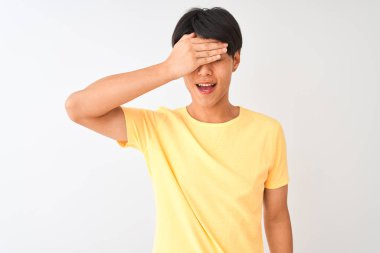 Izole beyaz arka plan üzerinde duran sarı rahat t-shirt giyen Çinli adam gülümseyerek ve sürpriz için gözleri kaplayan yüzünde el ile gülüyor. Kör kavramı.