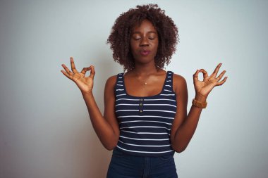 Genç afrikalı afro kadın çizgili t-shirt izole beyaz arka plan üzerinde duran dinlenmek ve gözleri parmakları ile meditasyon jest yapıyor kapalı gülümseyerek giyiyor. Yoga konsepti.
