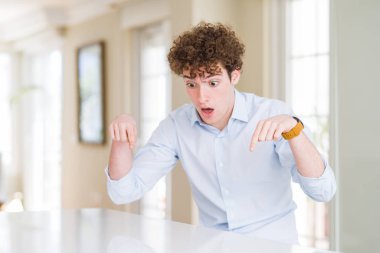 Kıvırcık okunan genç iş adamı Reklam gösteren parmakları ile aşağı işaret, sürpriz yüz ve açık ağız