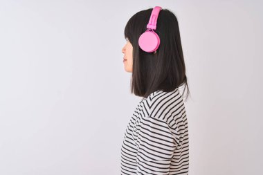 Çinli kadın yan bakarak izole beyaz arka plan üzerinde pembe kulaklık kullanarak müzik dinlerken, kendine güvenen gülümseme ile doğal yüz ile profil poz dinlenmek.