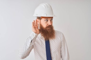 Genç kızıl İrlandalı mimar adam izole beyaz arka plan üzerinde güvenlik kask giyen el kulak üzerinden bir işitme dinleme ile gülümseyerek söylenti veya dedikodu. Sağırlık kavramı.