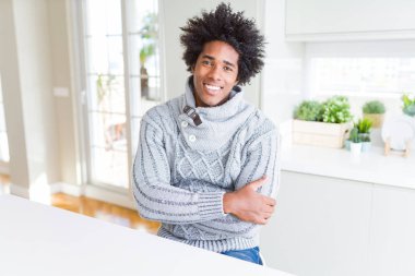 Kış lık kazak giyen Afro-Amerikan adam mutlu bir yüz le gülümseyerek kameraya bakıyor çapraz kollarıyla. Pozitif kişi.