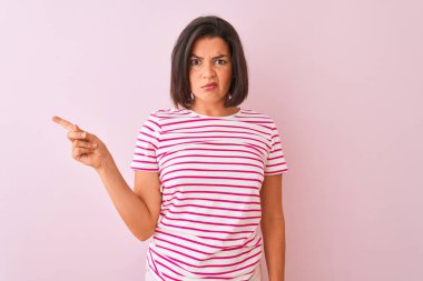 İzole pembe arka plan üzerinde duran çizgili t-shirt giyen genç güzel kadın işaret parmağı ile endişeli ve sinirli bir kenara işaret parmağı, endişeli ve sürpriz ifade