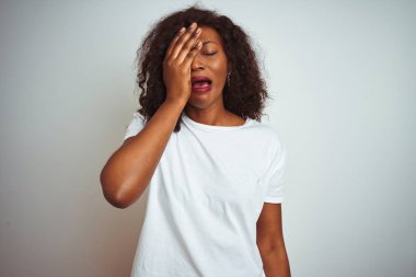 Genç afro-amerikan kadın izole beyaz arka plan üzerinde duran t-shirt giyen yawning yarım yüz kapsayan yorgun, göz ve el ile ağız. Yüz acı içinde acıyor.