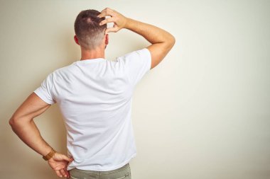 İzole arka plan geriye düşünme hakkında şüphe kafasına el ile üzerinden Casual beyaz t-shirt giyen genç yakışıklı adam