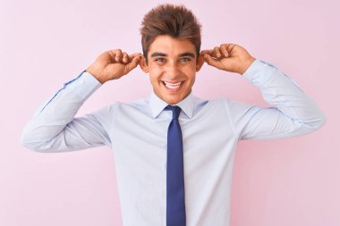 Genç yakışıklı işadamı gömlek ve kravat izole pembe arka plan üzerinde duran parmakları ile kulakları çekerek, komik jest giyiyor. Seçme sorunu