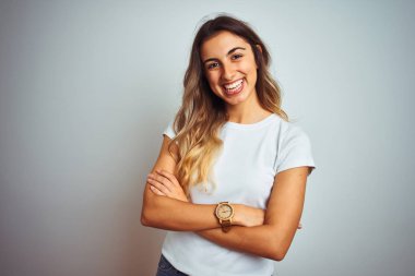 Izole arka plan üzerinde rahat beyaz t-shirt giyen genç güzel kadın kamera bakarak çapraz kolları ile gülümseyen mutlu yüz. Pozitif kişi.
