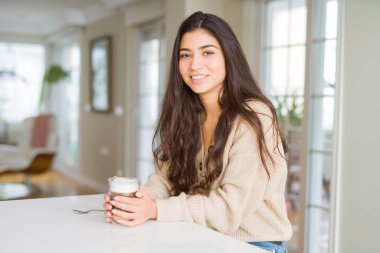 Güzel genç kız evde bir fincan kahve içme ve gülümseyerek