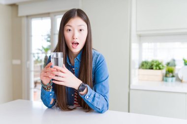 Güzel Asyalı kadın bir bardak tatlı su içerken şokta korkmuş sürpriz bir yüz, korku ve korku ifade ile heyecanlı