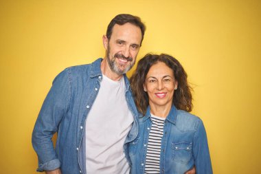 Güzel orta yaş çift birlikte yüzünde mutlu ve serin bir gülümseme ile izole sarı arka plan üzerinde denim gömlek giyiyor. Şanslı kişi.